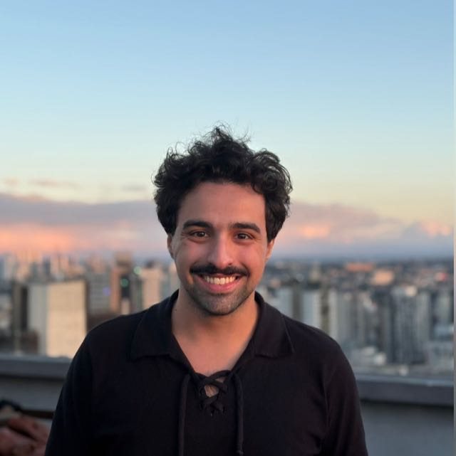 Guilherme Salamuni sorrindo, com a cidade de São Paulo ao fundo no fim de tarde
